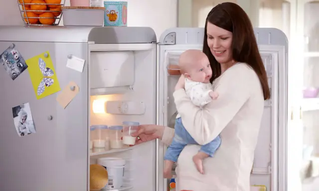 Mama z dzieckiem przy lodówce, gdzie przechowywanie mleka matki jest łatwe dzięki specjalnym pojemnikom.