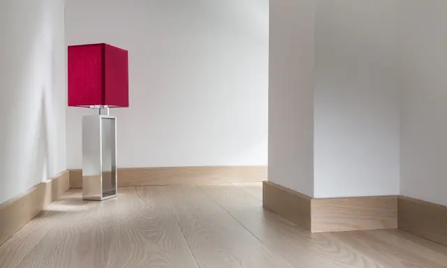 Enkel golvlistsinspiration i ljust trä som ramar in ett modernt rum med en röd bordslampa.