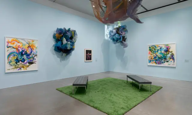 Abstract paintings and fabric sculptures adorn the walls of the Lanoue Gallery, with benches placed on a patch of artificial grass.