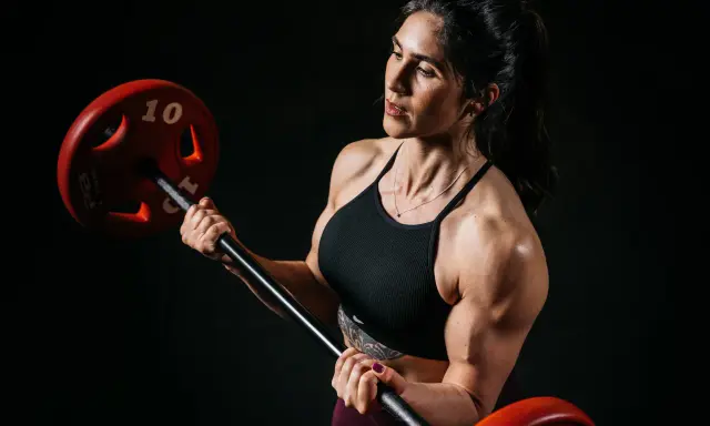 Eine starke Bodybuilderin Frau hebt eine Hantel. Ihre Muskeln sind deutlich sichtbar.