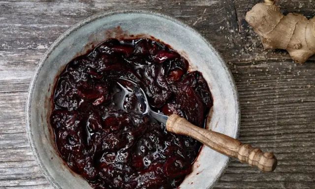 Dunkles, glänzendes Zwetschgen-Chutney in einer Schale, daneben ein Stück Ingwer und Zucker.