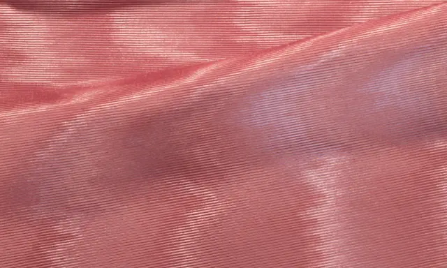 Tessuto rosa con pieghe che creano un affascinante effetto moiré, riflettendo la luce in modo cangiante.