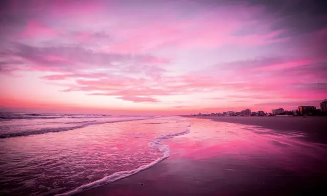 Spiaggia di Riccione immersa nel rosa della Notte Rosa, con il mare calmo e il cielo infuocato.