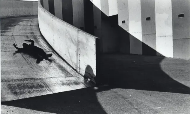 A silhouetted figure lies on a curved concrete ramp, arms outstretched, at the Janet Borden Gallery.