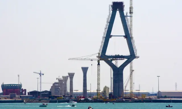 Construcción de un puente con pilares de hormigón y grúas, sobre el mar.