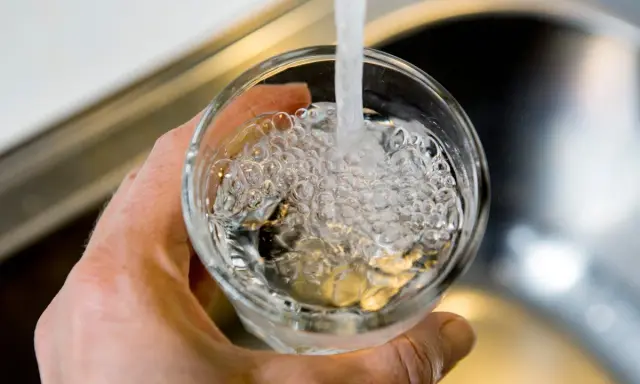 En hand håller ett glas som fylls med vatten från en kran. Bubblor bildas i vattnet, vilket kan tyda på klor i dricksvatten.