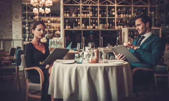 Elegancka para przegląda menu w luksusowej restauracji. On w granatowym garniturze, ona w czarnej sukni.