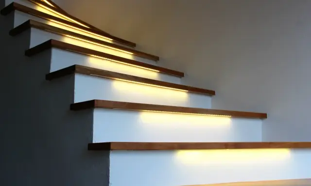 Nowoczesne lampy na klatkę schodową subtelnie oświetlają drewniane stopnie, tworząc ciepłą i bezpieczną atmosferę.