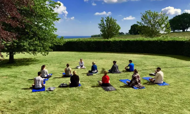Grupp med människor på en grön gräsmatta under en yoga retreat. En instruktör sitter framför gruppen.