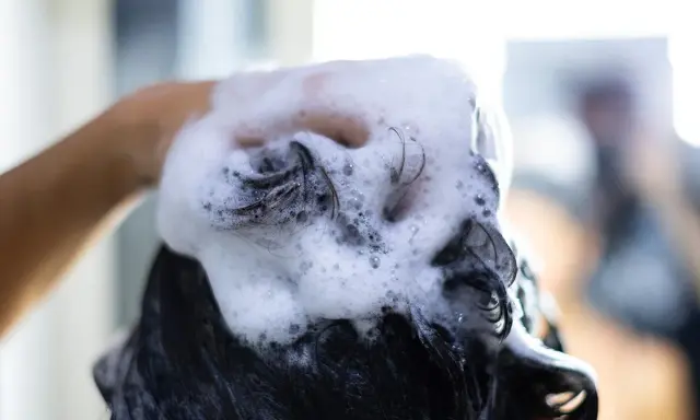 Mano che massaggia shampoo schiumoso sui capelli scuri, puliti o sporchi, per un momento di relax.