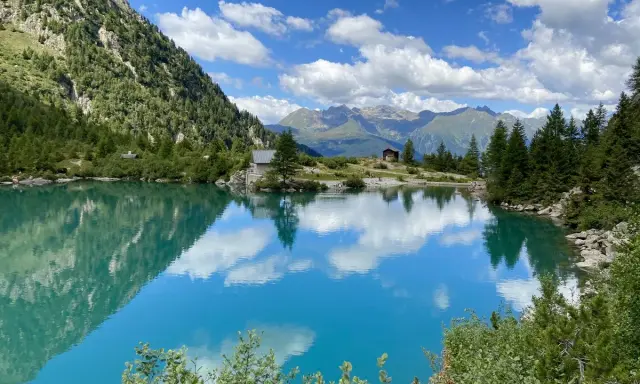 Lago alpino cristallino, perfetto per passeggiate in montagna Lombardia. Riflessi di cielo e montagne.