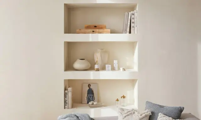 Una nicchia nel muro del salotto, con libri, vasi e diffusore, crea un angolo accogliente e ordinato.