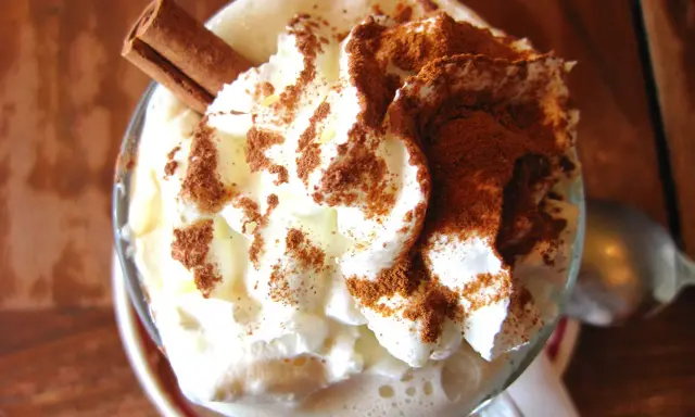 Un déliceux café liégeois recette : crème fouettée, cacao et bâton de cannelle dans un verre.