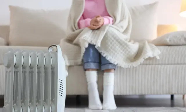 Radiador eléctrico junto a un sofá donde una persona se abriga. Una solución eficaz para los sistemas de calefacción del hogar.