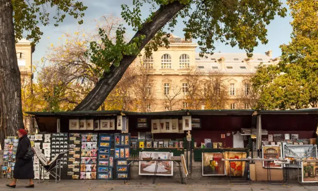 Ein Stand auf dem **Flohmarkt Paris** mit Postkarten, Büchern und Gemälden vor einem historischen Gebäude.