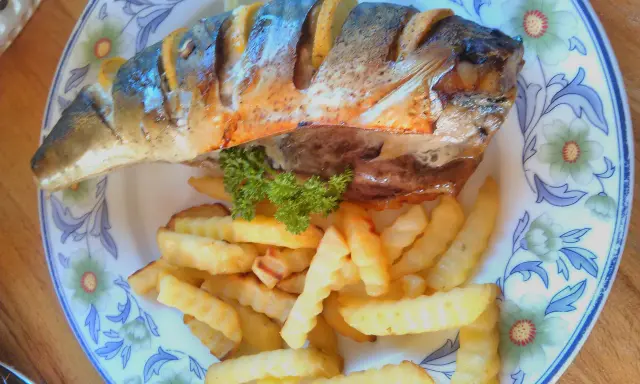 Pyszna makrela pieczona z cytryną i chrupiącymi frytkami, udekorowana natką pietruszki, na talerzu z kwiatowym wzorem.