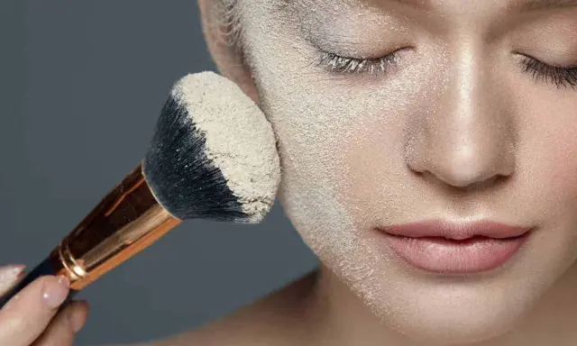 Applicazione di cipria per il baking trucco su un viso, con un pennello carico di prodotto.