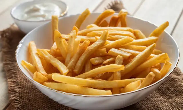Chrupiące frytki z airfryer w białej misce, obok sos. Idealna przekąska na szybki obiad.