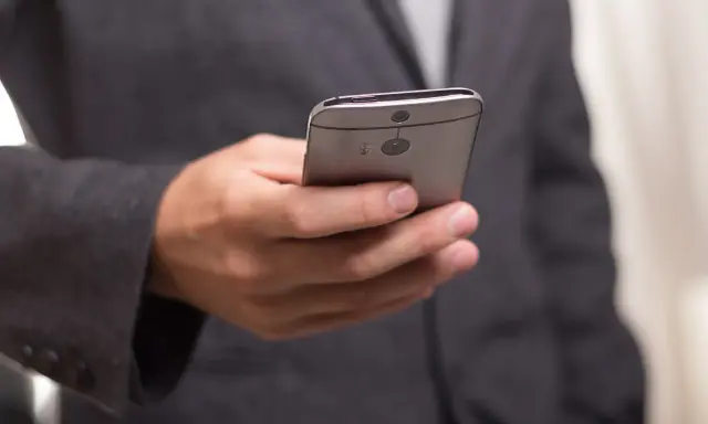 Mężczyzna w garniturze trzyma telefon, być może otrzymuje wiadomość o zawieszeniu działalności.