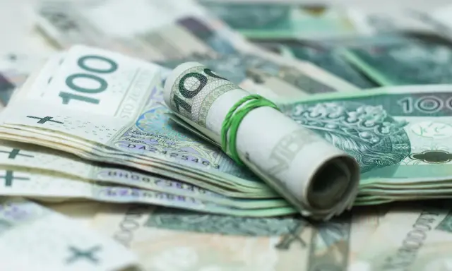 Zrolowane banknoty 100 zł, gotowe do spłaty zadłużenia u komornika przez osobę trzecią.