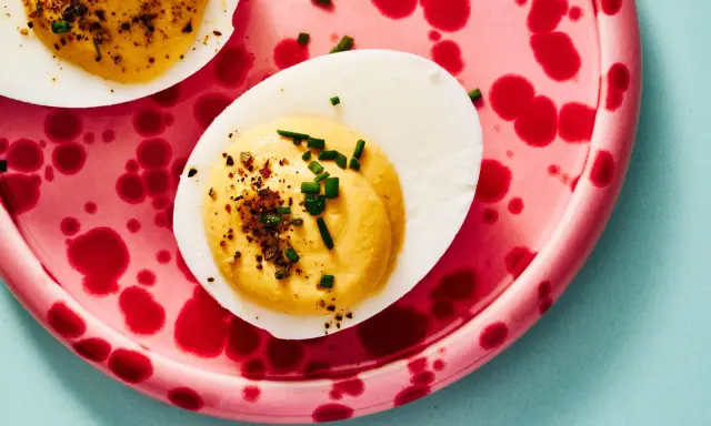 Deviled eggs deutsch: halbe hartgekochte Eier mit cremiger Füllung, bestreut mit Schnittlauch und Gewürzen, auf einem pinkfarbenen Teller mit roten Tupfen.