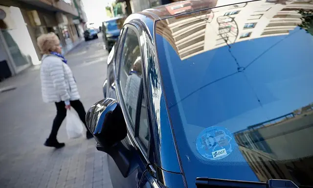 Una mujer cruza la calle mientras un coche eléctrico, con distintivo DGT, espera. Los coches eléctricos pagan zona azul.