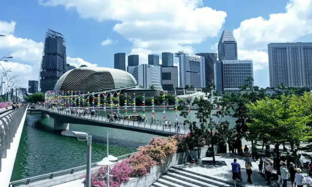 Fakta om Singapore: En bro med flaggor leder mot en futuristisk skyline med Esplanade-teatern.