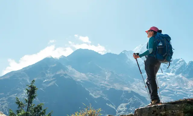Kobieta z plecakiem i kijkami trekkingowymi podziwia majestatyczne góry podczas trekkingu do Everest Base Camp.