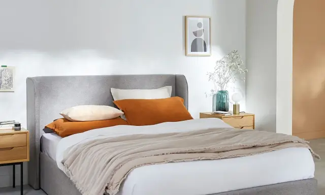 Cama gris con cojines naranjas y beige, perfecta para organizar canapé y crear un ambiente acogedor.