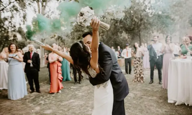 Novios besándose con humo verde, ¡ideas para una boda diferente! Invitados aplauden y celebran.