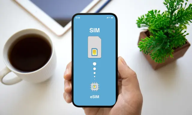 Dłoń trzyma smartfon z ekranem pokazującym proces aktywacji eSIM. Obok kubek kawy i roślinka.