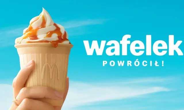 Lody McDonald's w wafelku z polewą karmelową, trzymane w dłoni na tle błękitnego nieba.