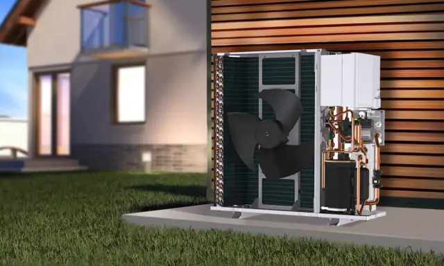 Unidad exterior de bomba de calor para hidrotermia en casa, con ventilador y tuberías de cobre visibles, junto a una casa moderna.