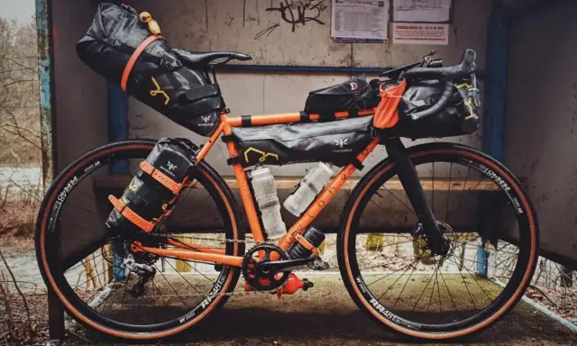 Orange Rennrad mit Bikepacking-Taschen, bereit für Abenteuer.