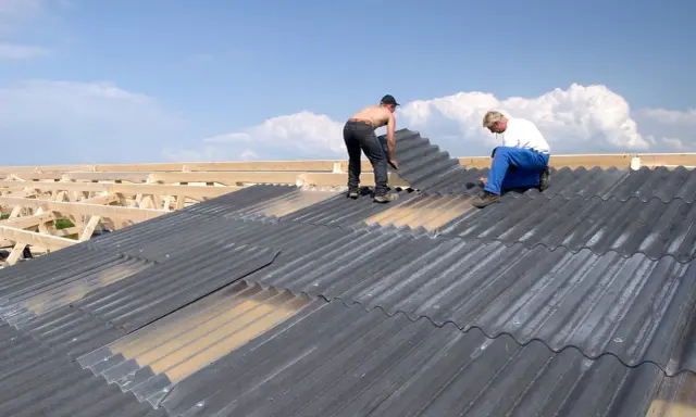 Zwei Handwerker sanieren ein Eternitdach. Die Kosten für die Sanierung eines Eternitdachs sind oft eine wichtige Überlegung.