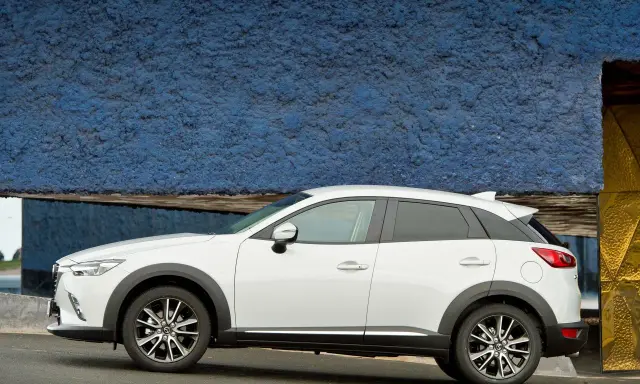 Biała Mazda CX-3 na tle niebieskiej ściany. Sprawdź aktualną mazda cx3 cena i wybierz swój wymarzony samochód.