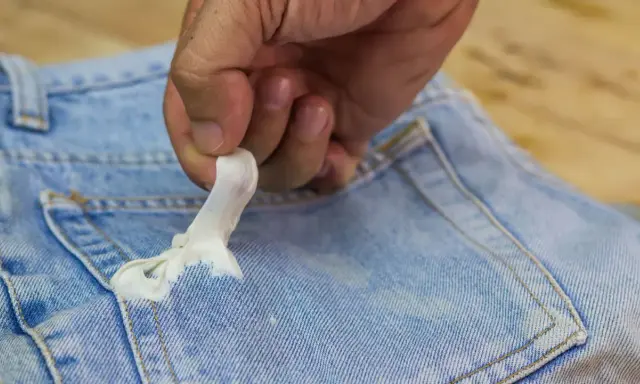 Mano quitando chicle pegado en un bolsillo de jeans. Aprende cómo quitar chicle de la ropa fácilmente.