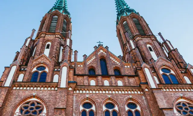 Dwie wieże ceglanego kościoła z zielonymi iglicami, jeden z najpiękniejszych kościołów w Polsce, pod błękitnym niebem.