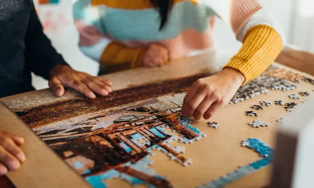 Dwie osoby składają puzzle, tworząc obraz. To dowód na to, że najlepsi producenci puzzli tworzą dzieła, które łączą ludzi.