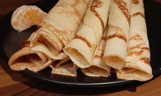 Crêpes à la bière roulées, dorées et légères, servies sur une assiette noire avec un quartier d'orange. Un délice !