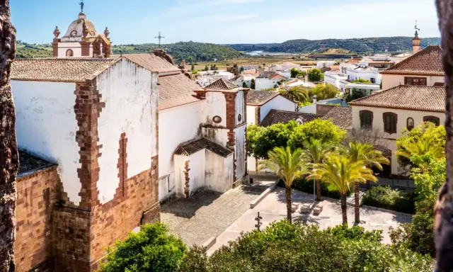 Blick über die weißen Häuser und Palmen von Silves, Portugal, mit einer Kirche im Vordergrund.