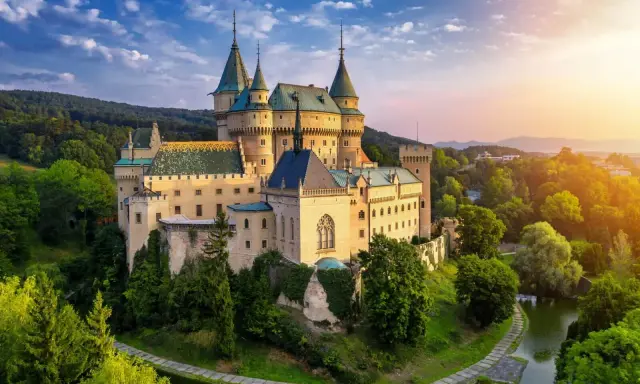 Bajkowy zamek otoczony zielenią, idealne miejsce na nocleg w zamku. Słońce zachodzi nad wzgórzami, tworząc magiczną atmosferę.