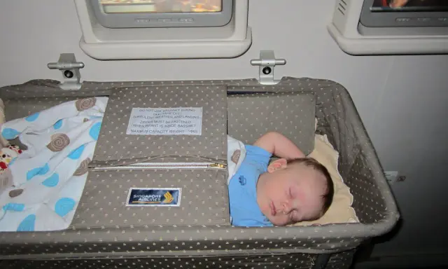 Śpiące dziecko w wózku dla dziecka Singapore Airlines podczas lotu. Wygodny enter air wózek dla dziecka zapewnia spokojny sen maluchowi.