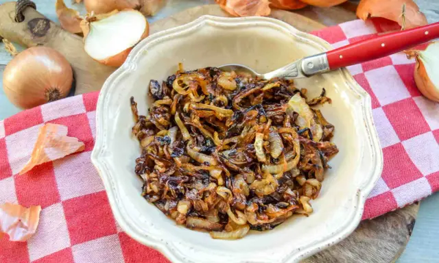 Schüssel mit karamellisierten Zwiebeln, die auf einem karierten Tuch liegen. Ganze und halbierte Zwiebeln sind daneben zu sehen.