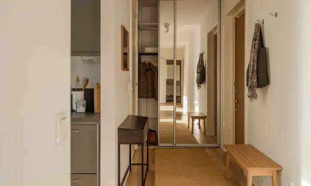 En ljus hall med spegelskjutdörrar, en smal konsol, en träbänk och en matta. Perfekt hall inspiration för en funktionell och stilren entré.