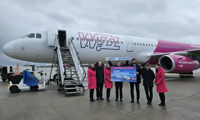 Grupa osób pozuje przed samolotem Wizz Air, trzymając tablicę z informacją o nowych trasach, w tym lotach Szczecin-Bergen.