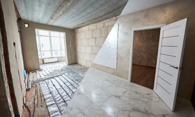 Habitación en construcción con suelo de mármol y sistema de calefacción por suelo radiante. El alicatado que es, se ve en el suelo y en la pared.
