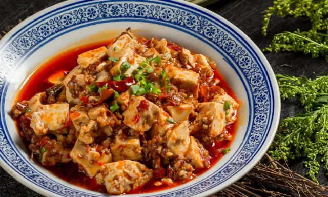 Pikantne tofu w sosie chili, klasyka kuchni syczuańskiej. Danie wygląda apetycznie, ozdobione szczypiorkiem.