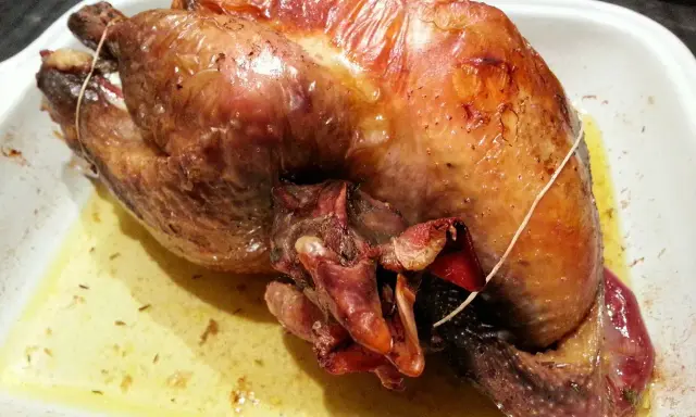 Une pintade au four, dorée et juteuse, repose dans un plat blanc, baignant dans son jus savoureux.