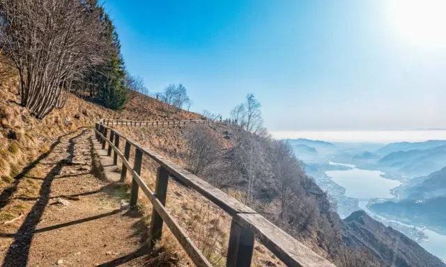Sentiero sul monte Coltignone con vista panoramica su un lago e montagne nebbiose.